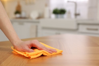 Woman with microfiber cloth cleaning wooden table in kitchen, closeup. Space for text