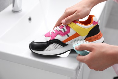 Photo of Woman washing stylish sneakers with brush in sink, closeup