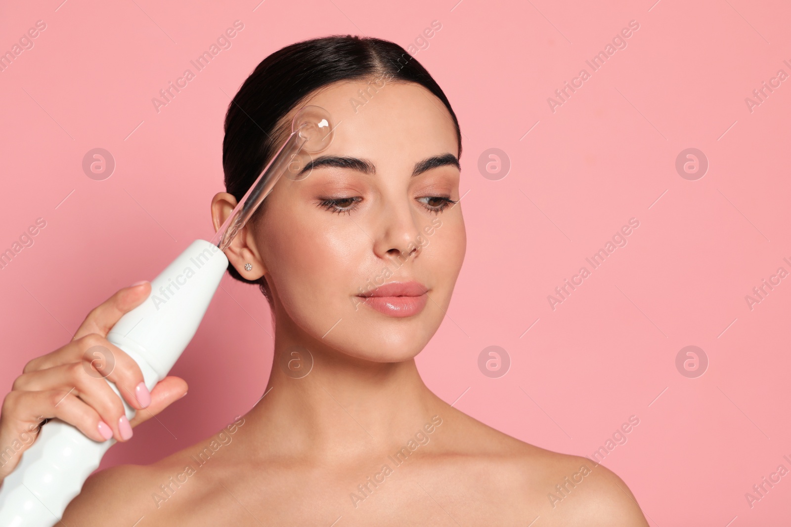 Photo of Woman using high frequency darsonval device on pink background. Space for text