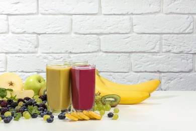 Photo of Fresh colorful fruit smoothies and ingredients on table against white brick wall. Space for text
