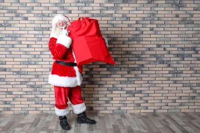 Photo of Authentic Santa Claus with big red bag full of gifts near brick wall