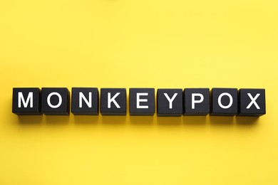Photo of Word Monkeypox made of black wooden cubes on yellow background, top view