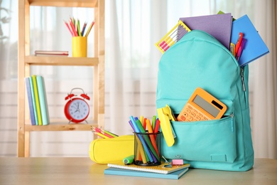 Photo of Bright backpack and school stationery on table indoors, space for text