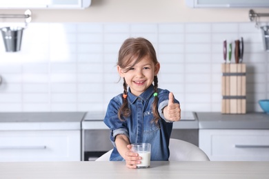 Photo of Cute little girl with glass of milk at table in kitchen