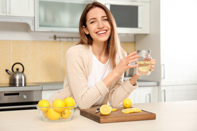 Young woman with mason jar of lemon water in kitchen