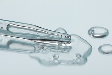 Photo of Glass pipette and transparent liquid on light background, closeup
