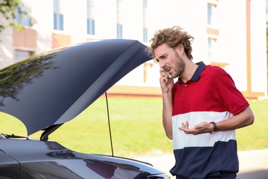 Photo of Young man talking on phone near broken car, outdoors