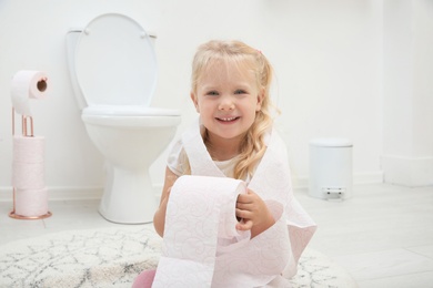 Photo of Cute little girl playing with toilet paper in bathroom
