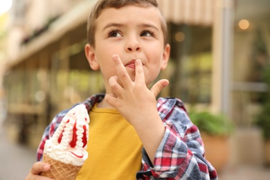 Photo of Adorable little boy with delicious ice cream outdoors