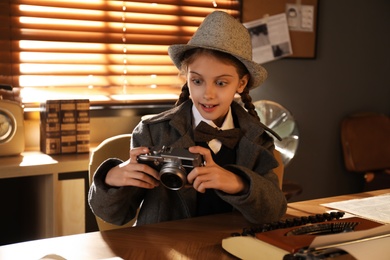 Photo of Cute little detective with camera at table in office