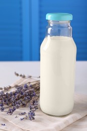 Photo of Bottle of tasty milk and lavender flowers on table against light blue wall, closeup