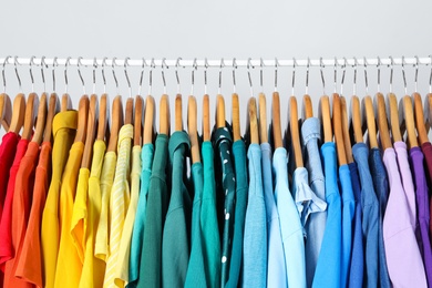 Photo of Rack with bright clothes on light blue background. Rainbow colors