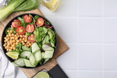 Photo of Tasty salad with chickpeas, cherry tomatoes and cucumbers served on white tiled table, flat lay. Space for text