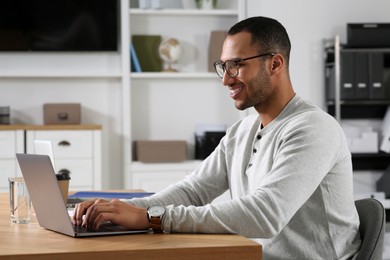 Photo of Young man working on laptop at table in office