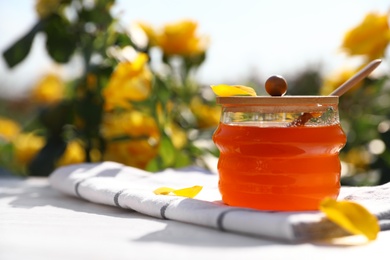 Photo of Jar with fresh rose honey on white wooden table outdoors. Space for text