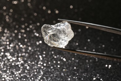 Photo of Tweezers with beautiful diamond on dark shiny background, closeup