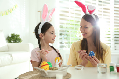 Happy mother and daughter with bunny ears headbands painting Easter eggs at home