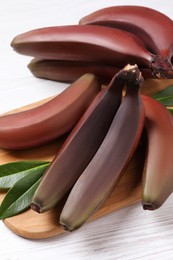 Photo of Tasty red baby bananas on white wooden table, closeup