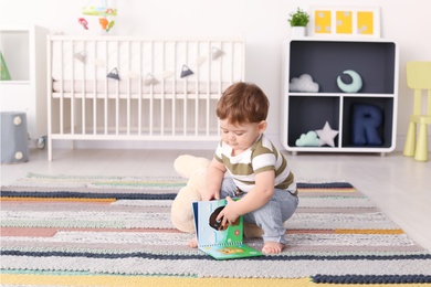 Photo of Cute baby sitting on floor with book at home