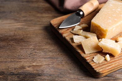 Photo of Parmesan cheese with knife on wooden table, closeup. Space for text