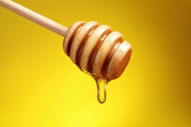 Photo of Delicious honey flowing down from dipper against yellow background, closeup