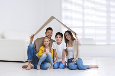 Photo of Happy family sitting under cardboard roof at home. Insurance concept