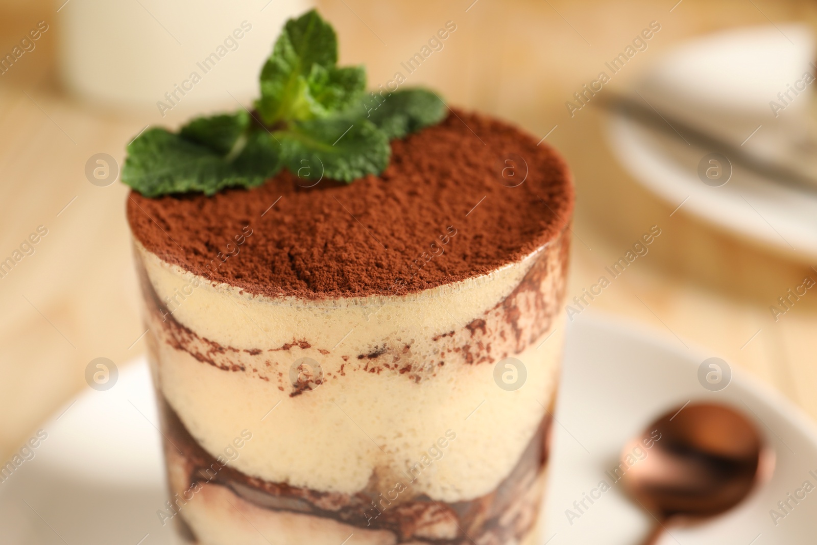 Photo of Tasty tiramisu and mint in glass on table, closeup