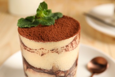Photo of Tasty tiramisu and mint in glass on table, closeup