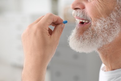 Photo of Senior man taking pill on blurred background, closeup view