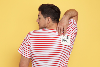 Photo of Man with APRIL FOOL sticker on back against yellow background
