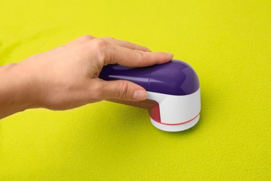 Photo of Woman cleaning light green cloth with fabric shaver, closeup