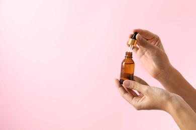 Photo of Woman with bottle of cosmetic serum and dropper on pink background, closeup. Space for text