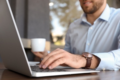 Image of Young man with cup of coffee working on laptop at outdoor cafe, closeup