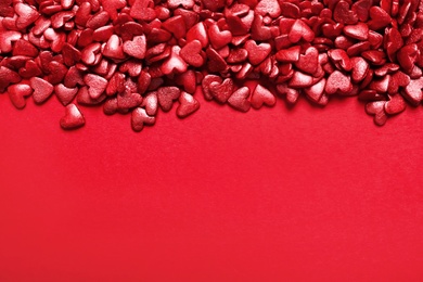 Photo of Bright heart shaped sprinkles on red background, view from above. Space for text