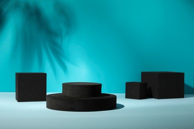 Photo of Many black geometric figures on light table against turquoise background, space for text. Stylish presentation for product