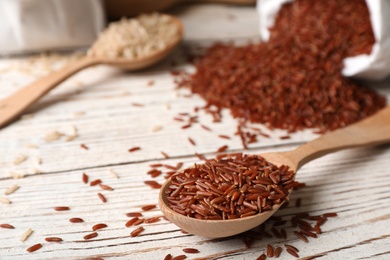 Photo of Uncooked brown rice in wooden spoon on table. Space for text