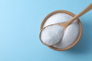 Photo of Organic white salt in bowl and spoon on light blue background, top view. Space for text