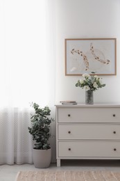 Photo of Chest of drawers and potted eucalyptus plant near window in room