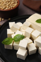Photo of Delicious tofu cheese, basil and soybeans on brown table, closeup