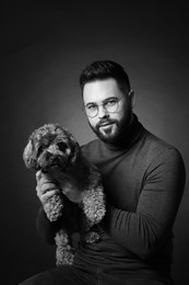 Photo of Handsome bearded man with cute dog on dark background. Black and white effect