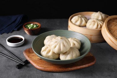 Photo of Delicious bao buns (baozi) in bowl on grey table, closeup