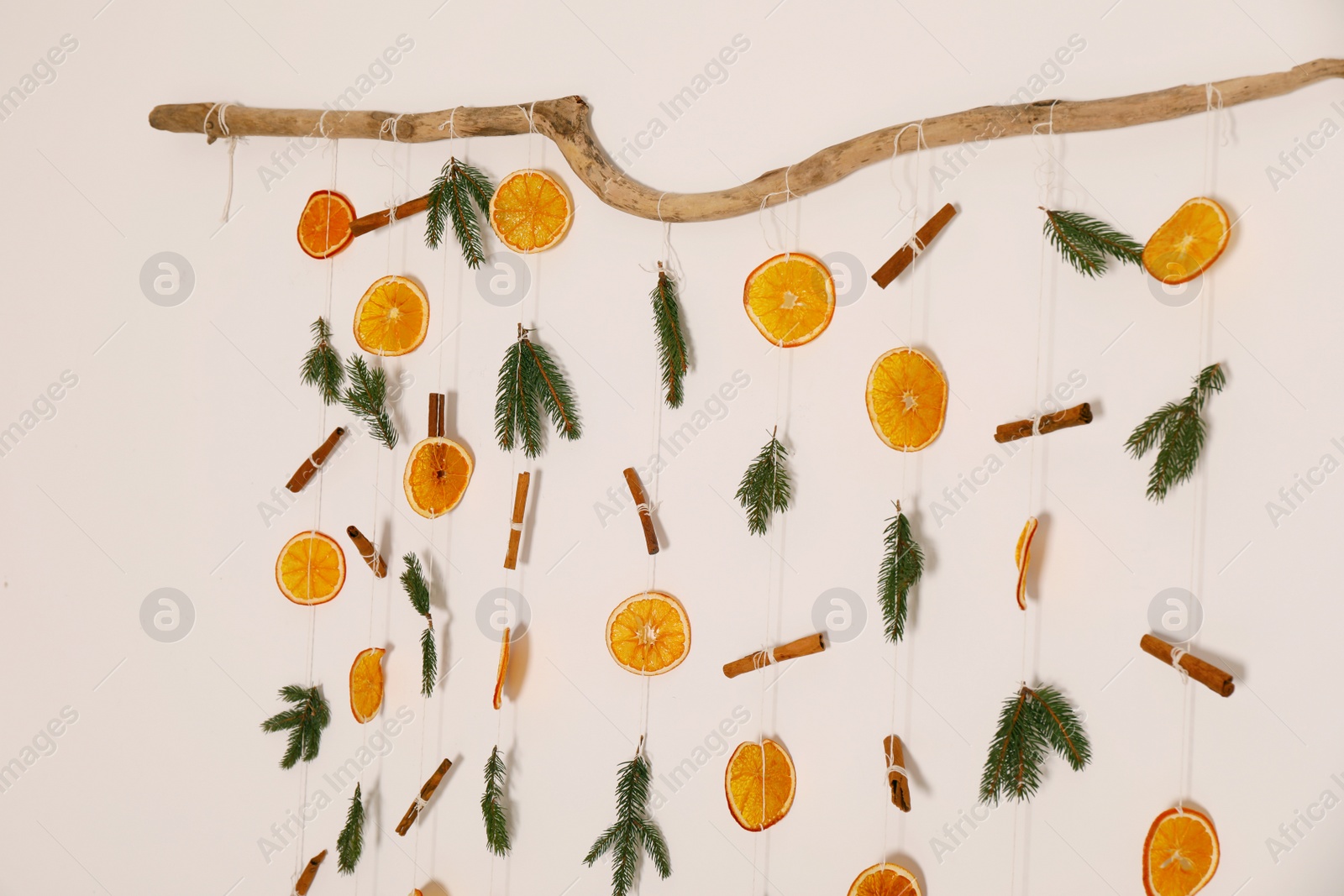 Photo of Handmade decor of dry orange slices, cinnamon sticks and fir tree branches on white wall, closeup