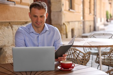 Photo of Handsome man with book working on laptop at table in outdoor cafe. Space for text