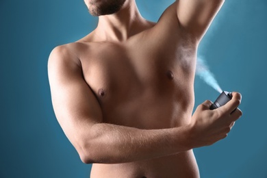 Photo of Young man using deodorant on color background, closeup