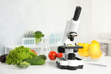 Photo of Microscope and fresh vegetables on table in laboratory. Poison detection