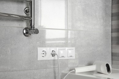Photo of Hairdryer plugged into power socket on light grey wall