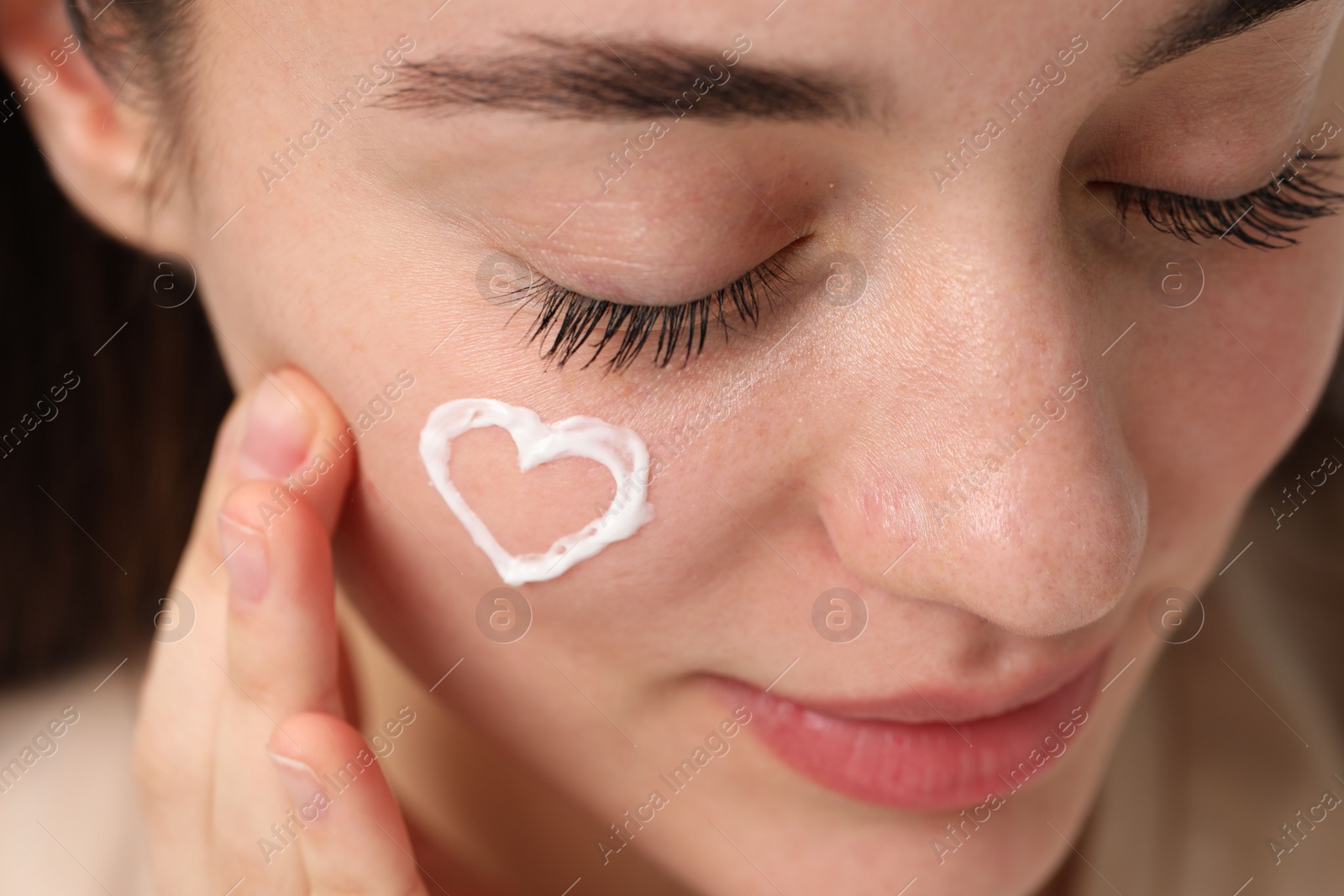 Photo of Young woman with dry skin and heart madecream on her face, closeup