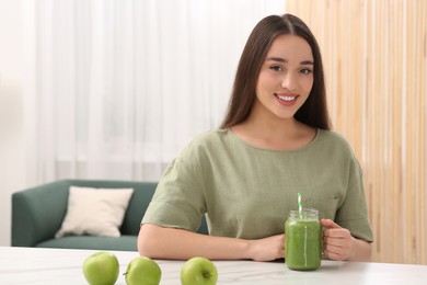 Photo of Beautiful young woman with mason jar of delicious smoothie and apples at home