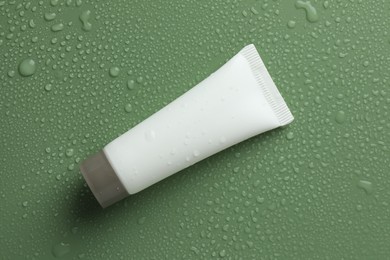 Photo of Moisturizing cream in tube on green background with water drops, top view