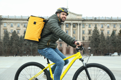 Photo of Courier with thermo bag riding bicycle outdoors. Food delivery service